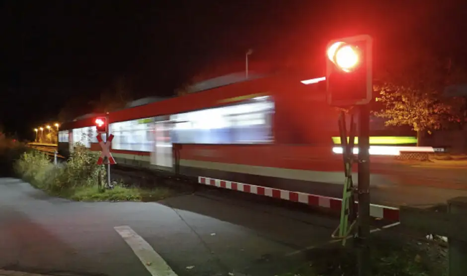 Ein Zug rauscht im Dunkeln an einem Bahnübergang vorbei
